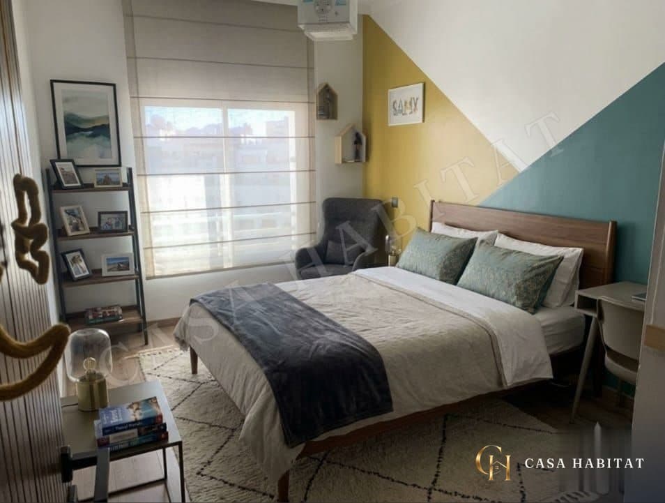 Chambre avec tête de lit en bois, murs jaune et bleu, fauteuil gris