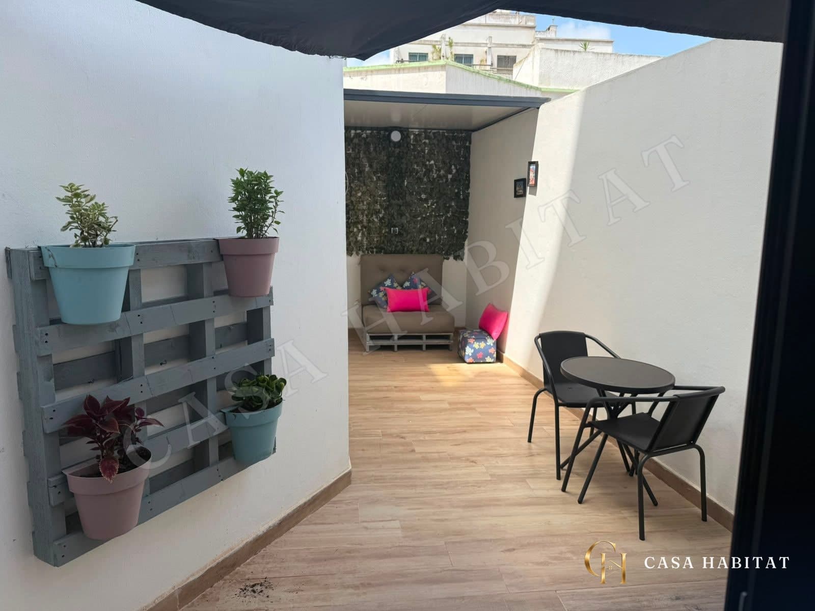 Terrasse carrelée avec table, chaises noires et jardinière en palette