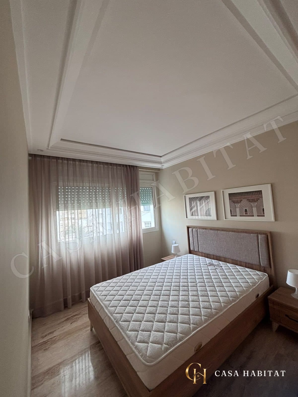 Chambre avec lit en bois, rideaux voilage et cadres muraux