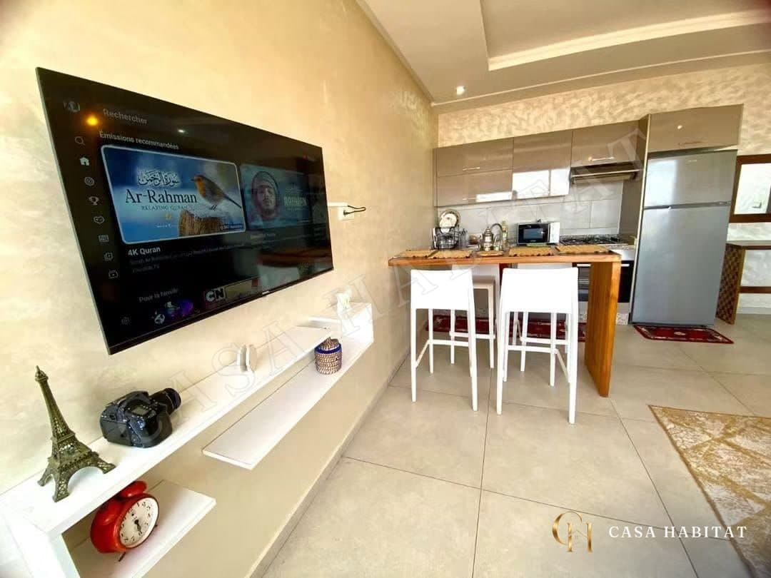 Coin TV et cuisine avec bar, tabouret blanc et réfrigérateur inox