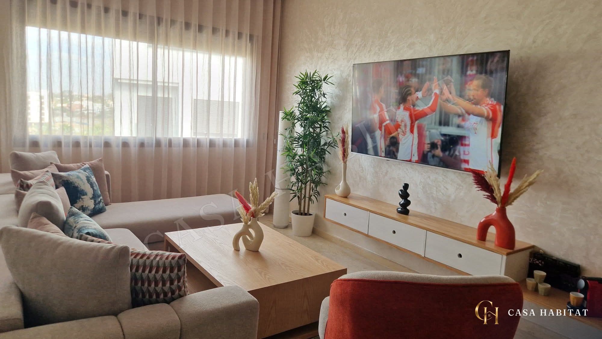 Salon avec canapé clair, coussins colorés et téléviseur fixé au mur