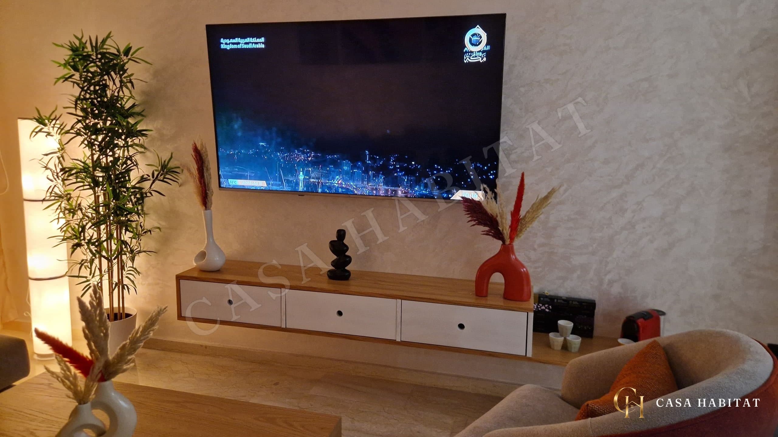Salon avec téléviseur mural, meuble bas en bois et fauteuil orange
