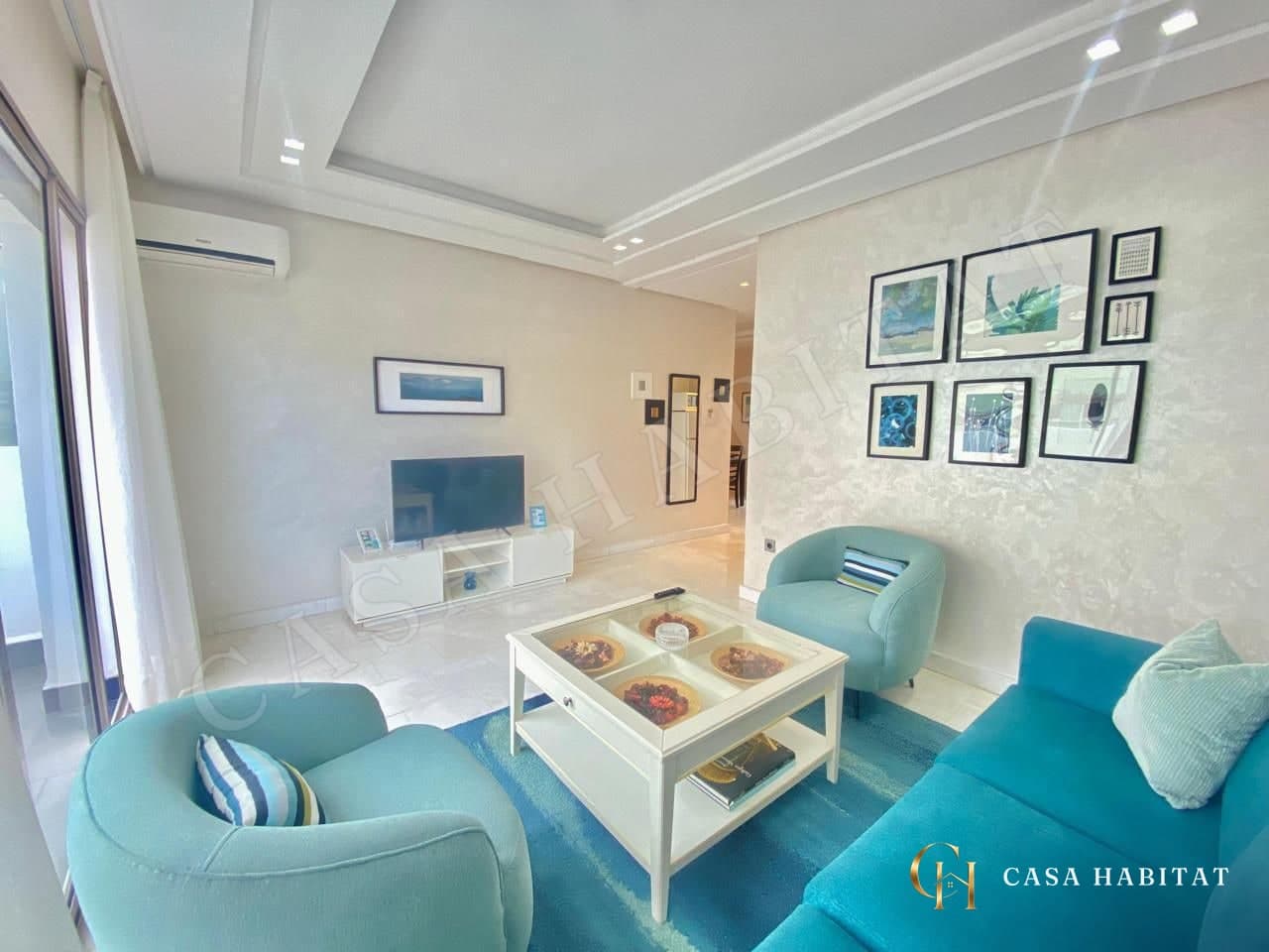 Salon avec fauteuils turquoise, meuble TV blanc et cadres muraux