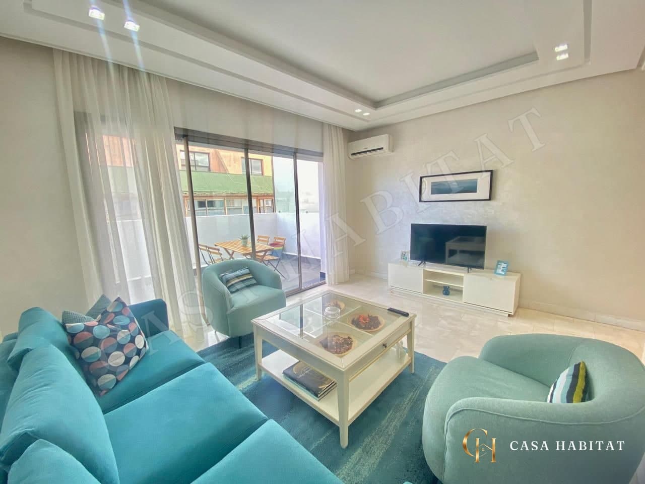 Salon avec canapé turquoise, fauteuils et baie vitrée sur terrasse