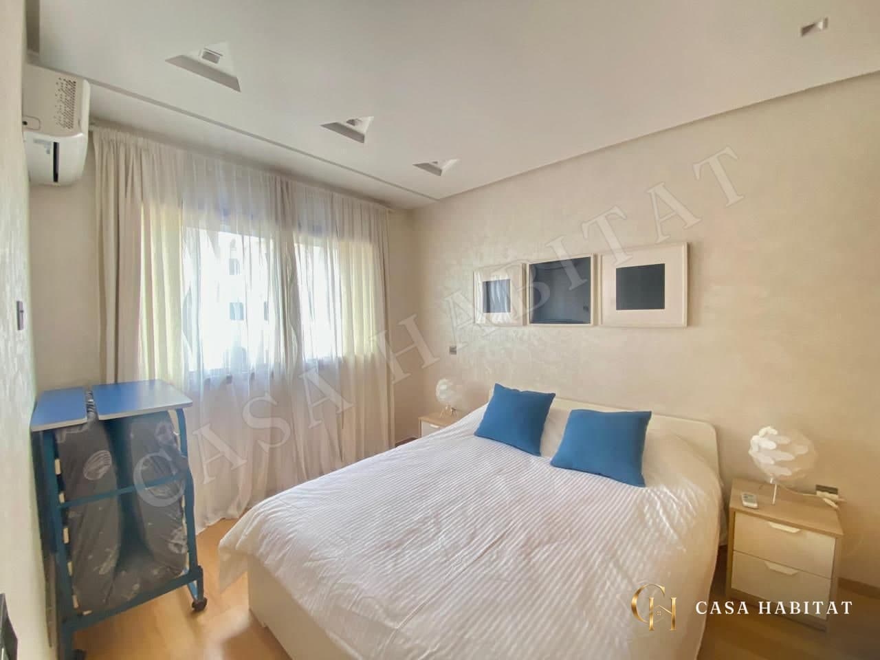 Chambre avec lit blanc, coussins bleus et fenêtre à rideaux