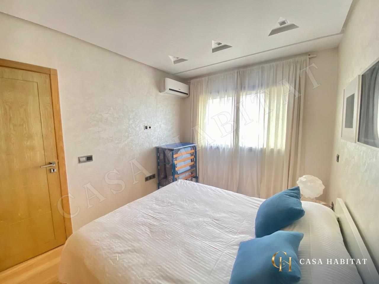 Chambre avec lit blanc, coussins bleus et climatiseur mural