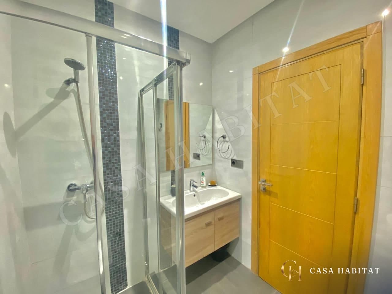 Salle d'eau avec douche en verre, lavabo et porte en bois