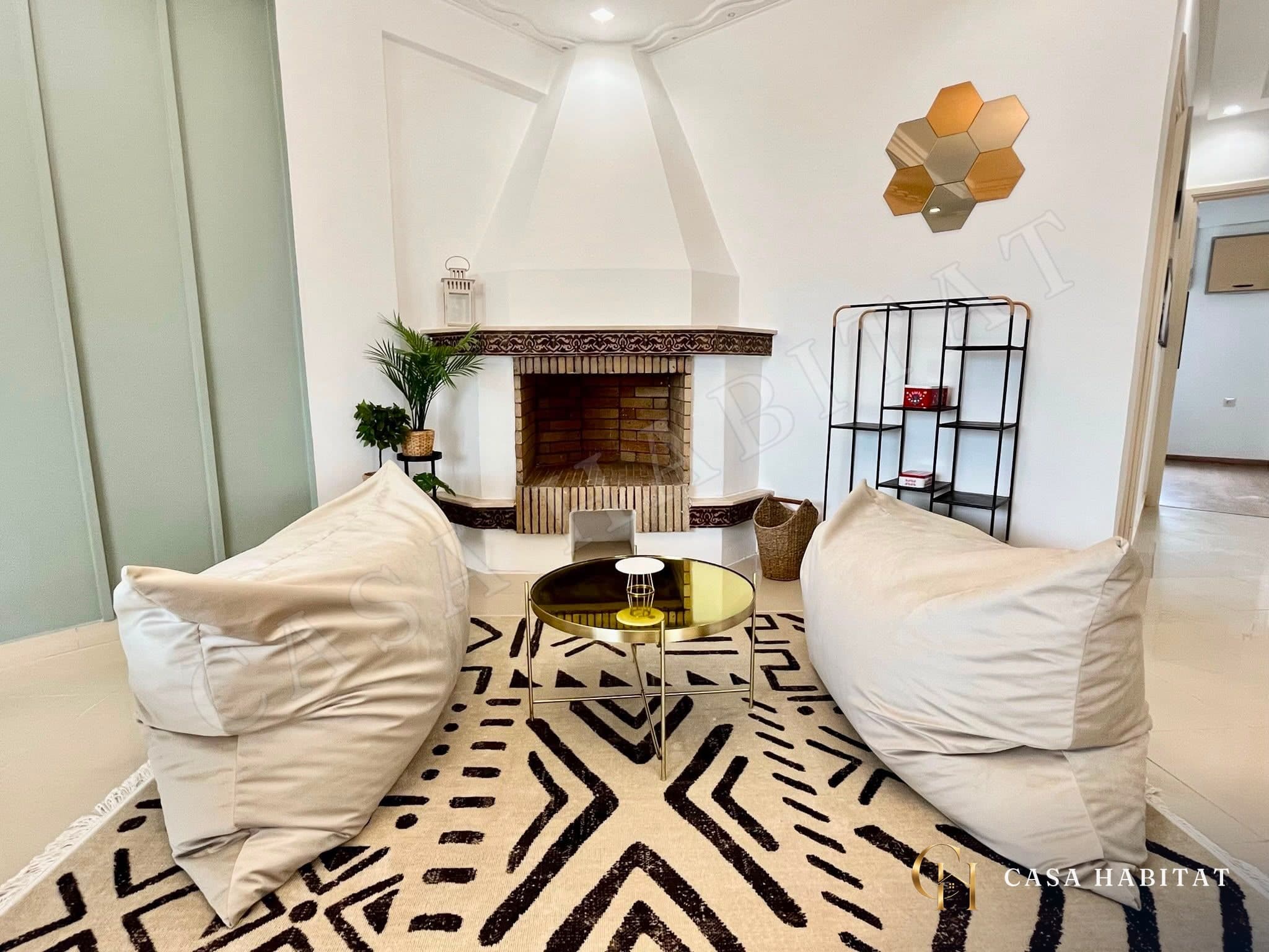 Coin salon avec deux poufs, table basse dorée et cheminée