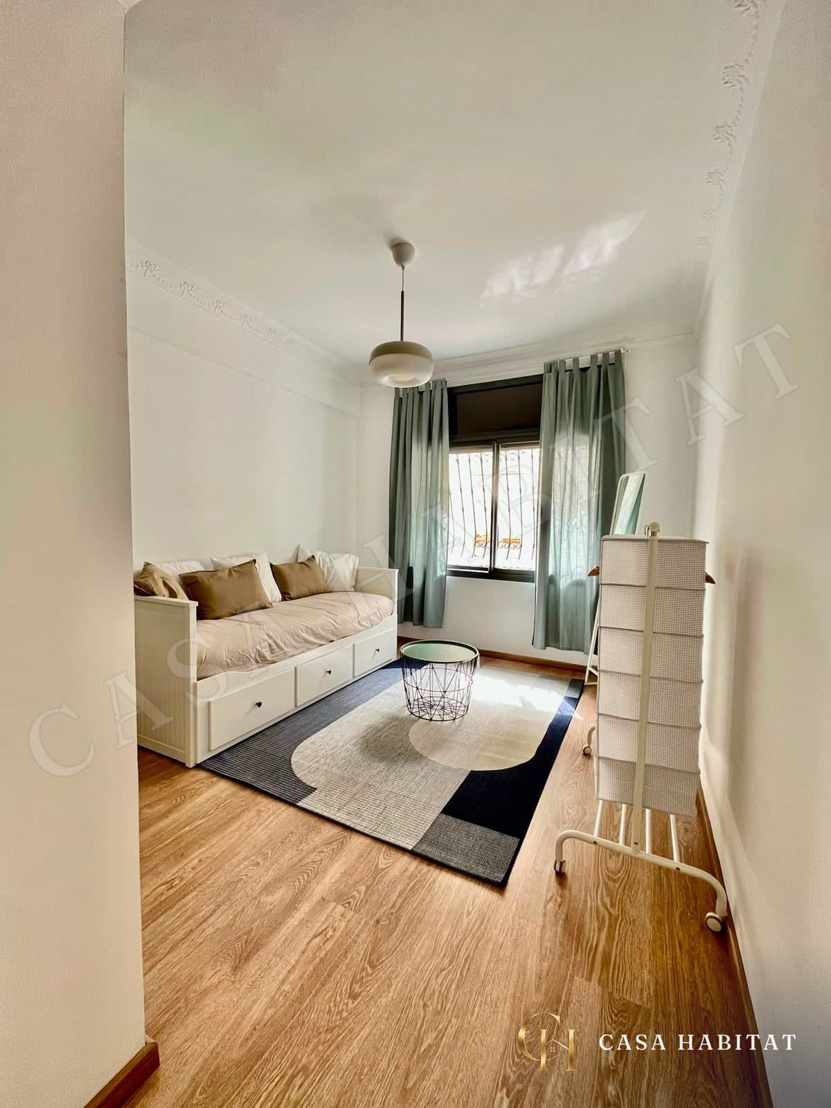 Chambre avec canapé-lit blanc, rideaux verts et parquet clair