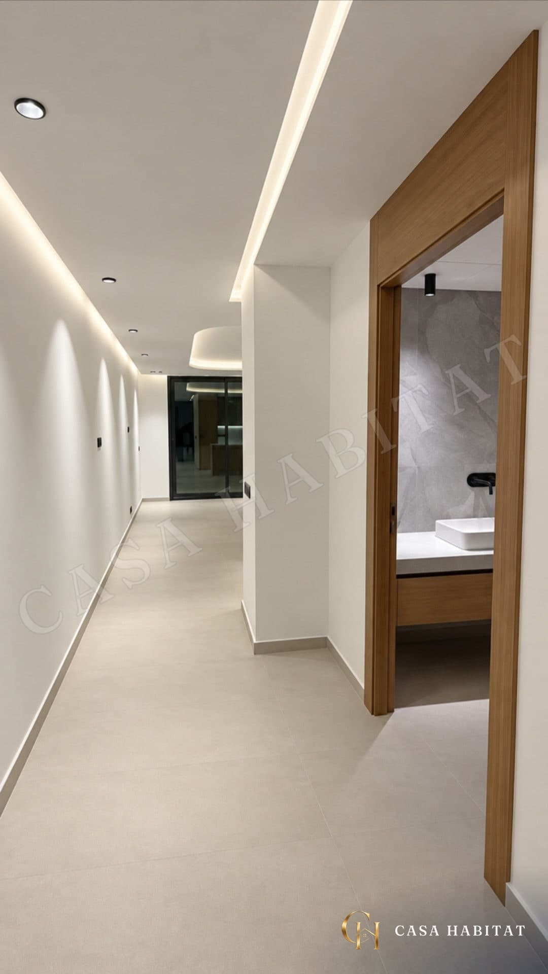 Couloir éclairé par spots, salle de bain en marbre à droite