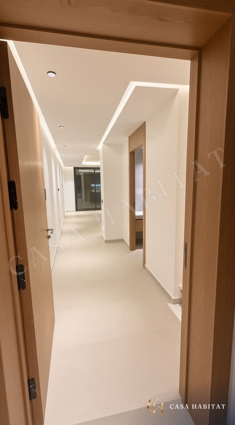 Couloir clair avec corniche lumineuse, porte en bois et salle de bain