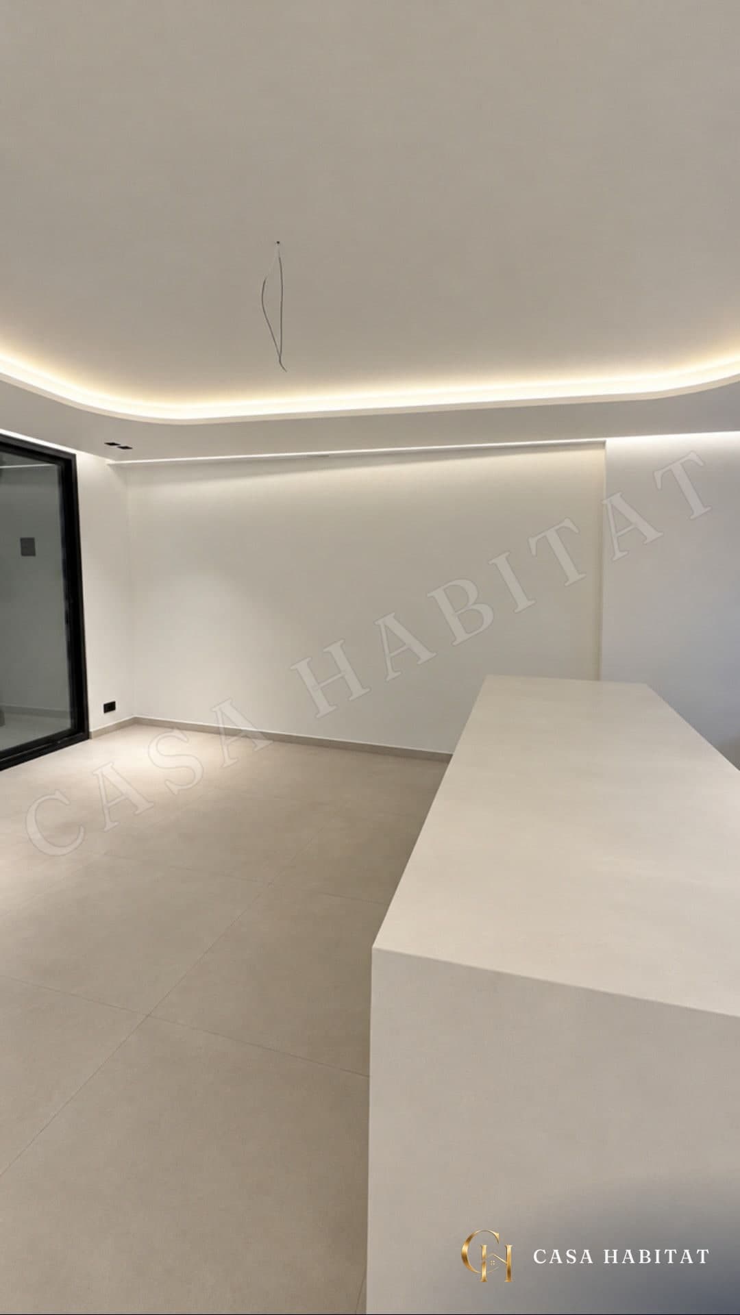 Pièce vide avec sol carrelé beige, plan de travail blanc et éclairage LED au plafond