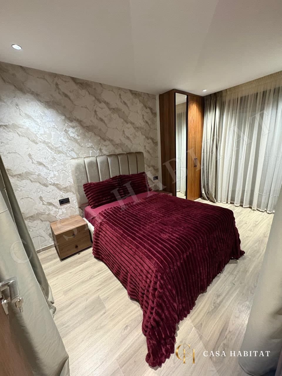 Chambre avec lit bordeaux, tête de lit capitonnée et penderie en bois