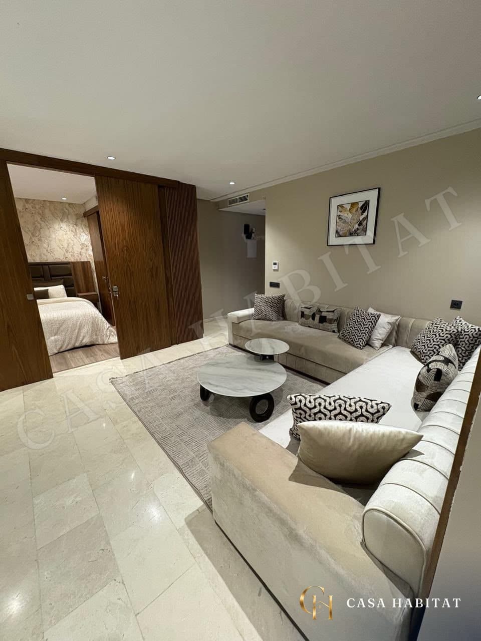 Salon avec canapé d'angle beige et accès à la chambre par porte coulissante