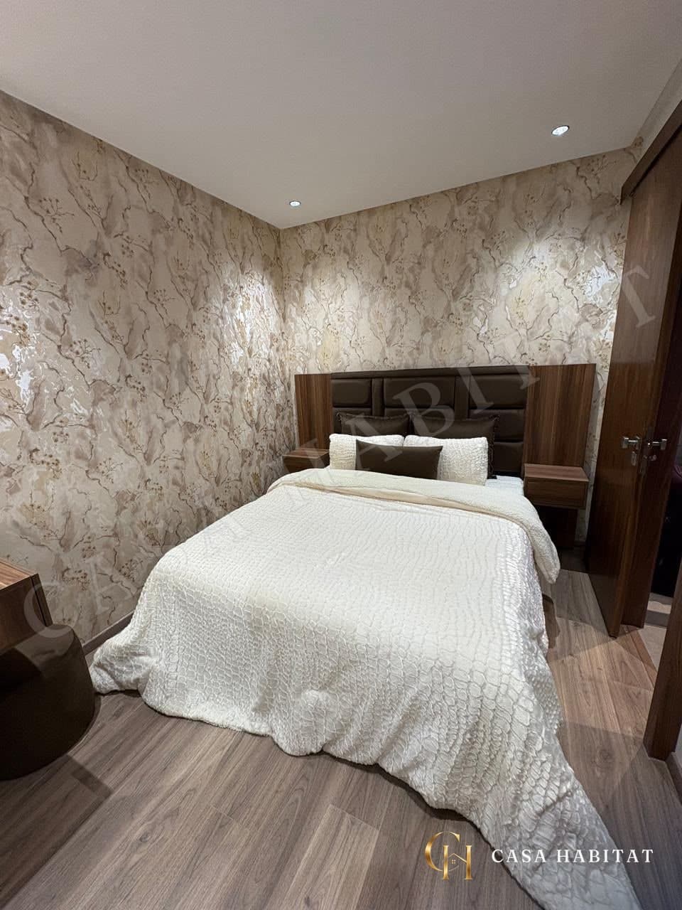 Chambre avec lit blanc, tête de lit brune et murs beige motifs