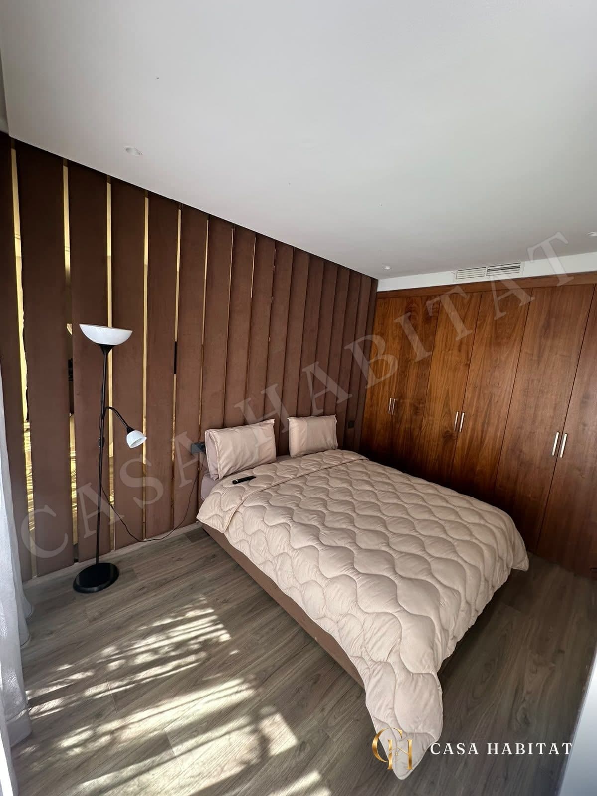 Chambre avec lit recouvert d'une couette beige et placard en bois