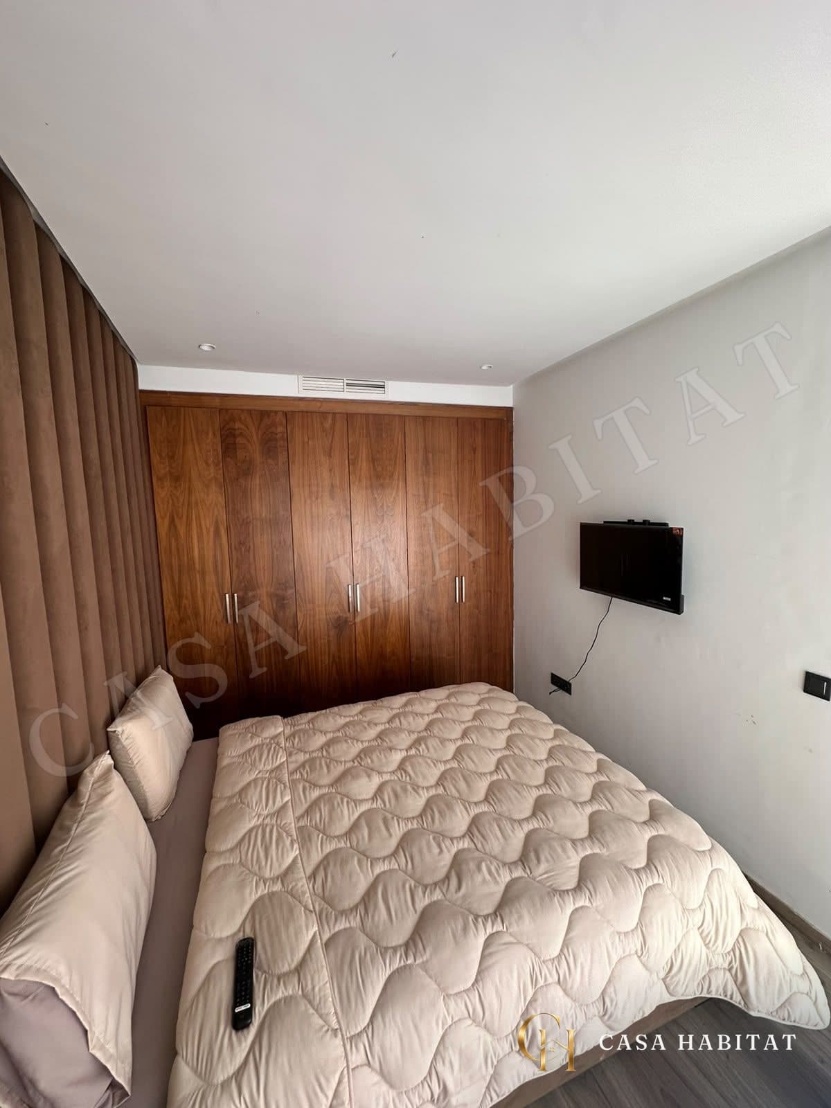 Chambre avec lit et placards en bois sous une bouche d'aération