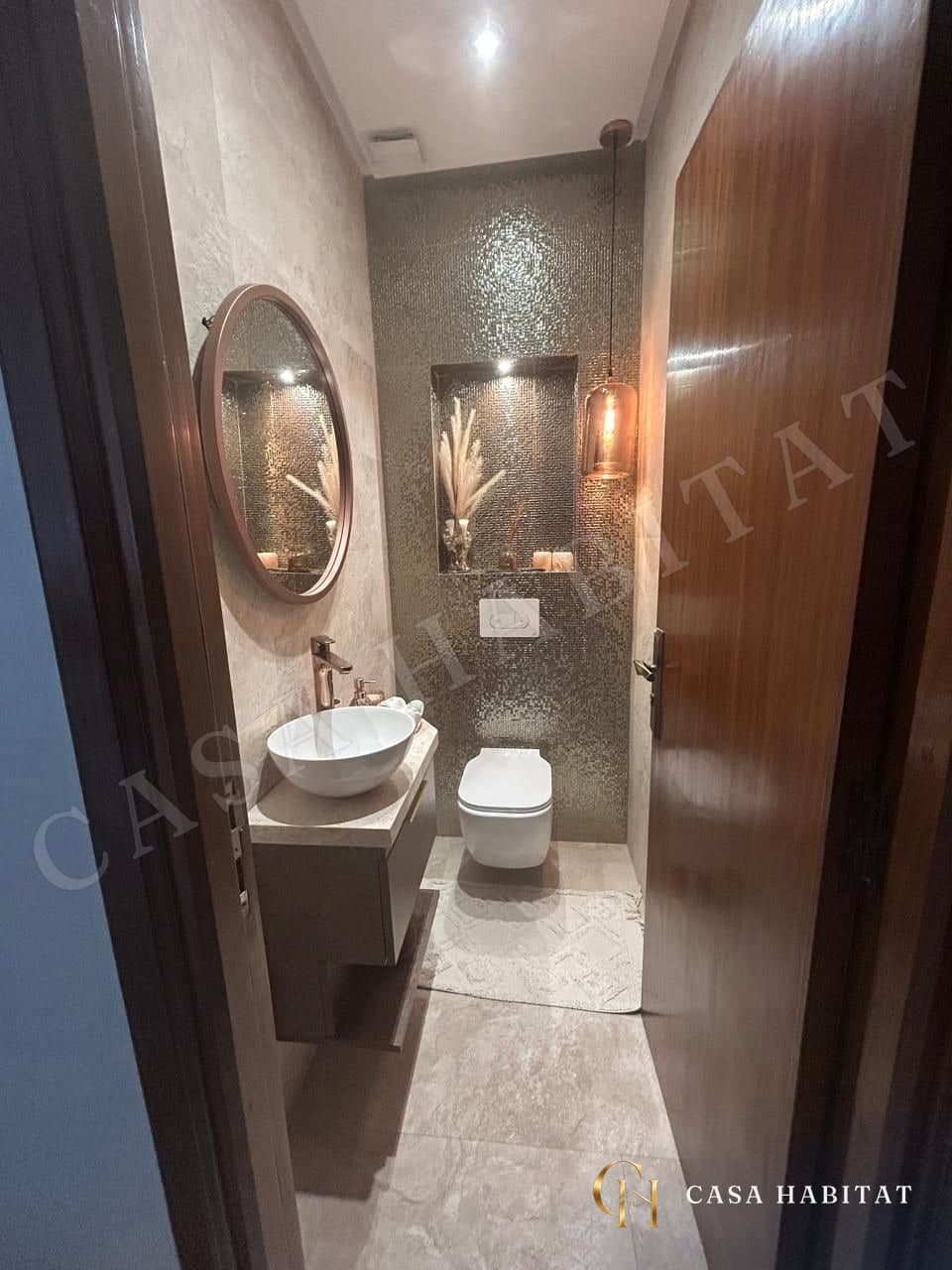 Toilettes avec vasque ronde, miroir rond et mosaïque dorée au mur