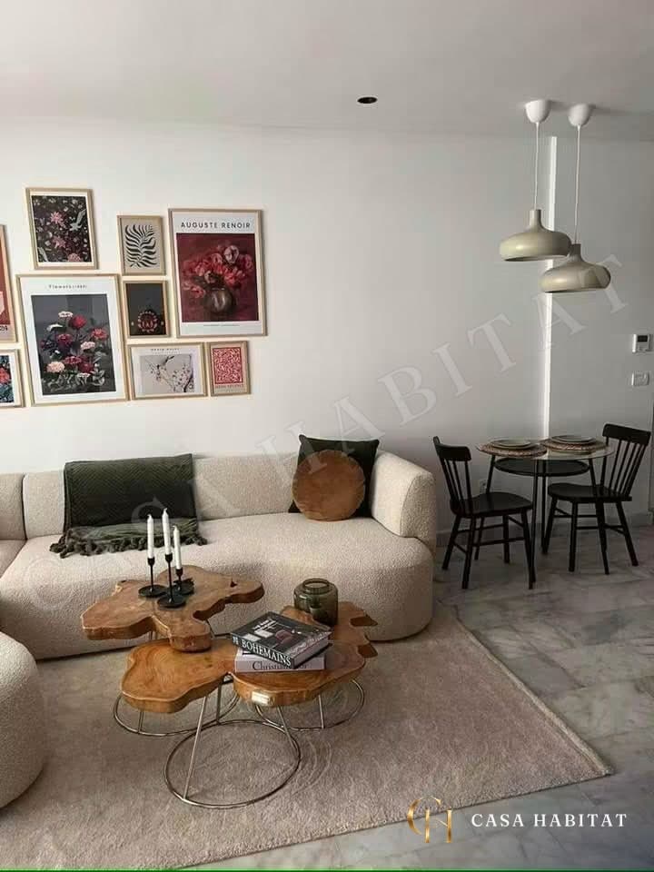 Salon avec canapé beige, cadres muraux et coin repas à droite