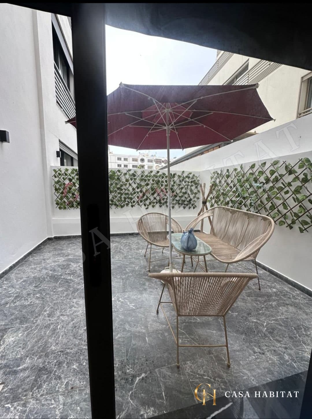 Terrasse avec parasol rouge et fauteuils en osier