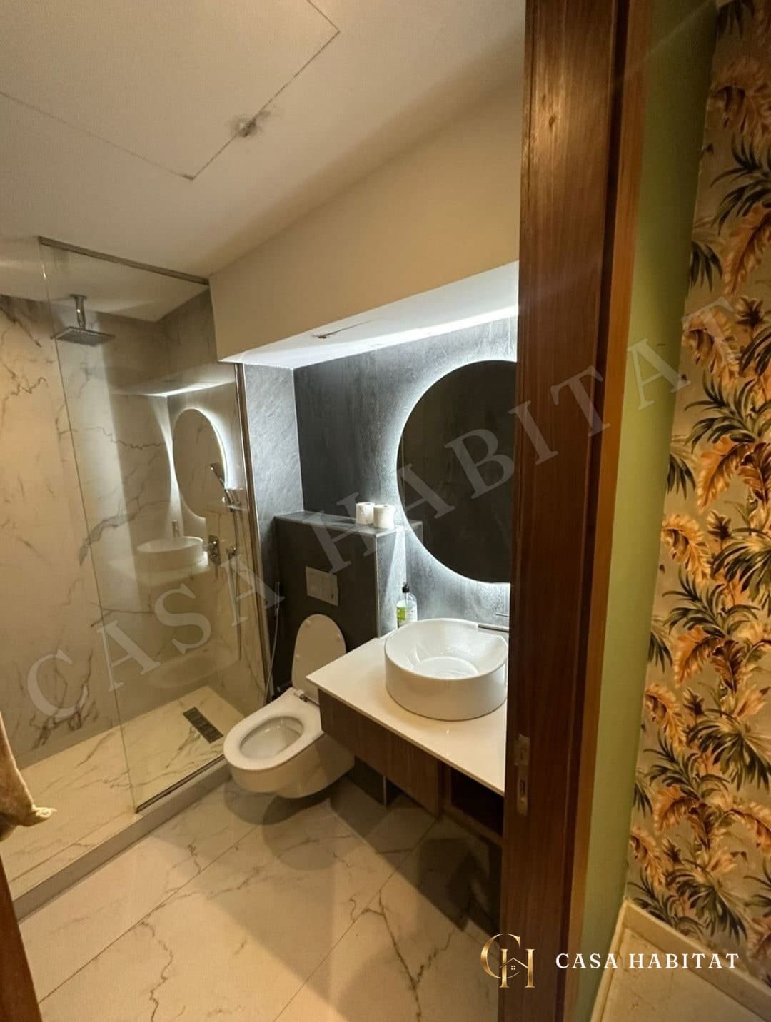 Salle de bain avec douche en verre, lavabo rond et miroir rond éclairé