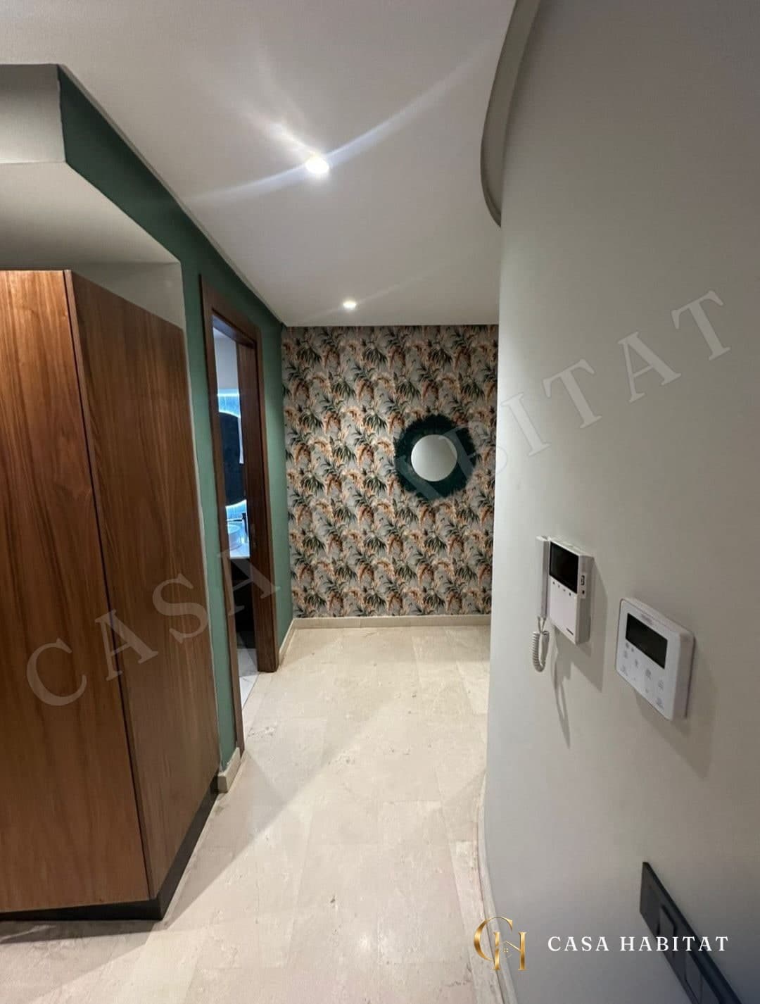 Couloir avec placard en bois, miroir rond et mur à motifs floraux