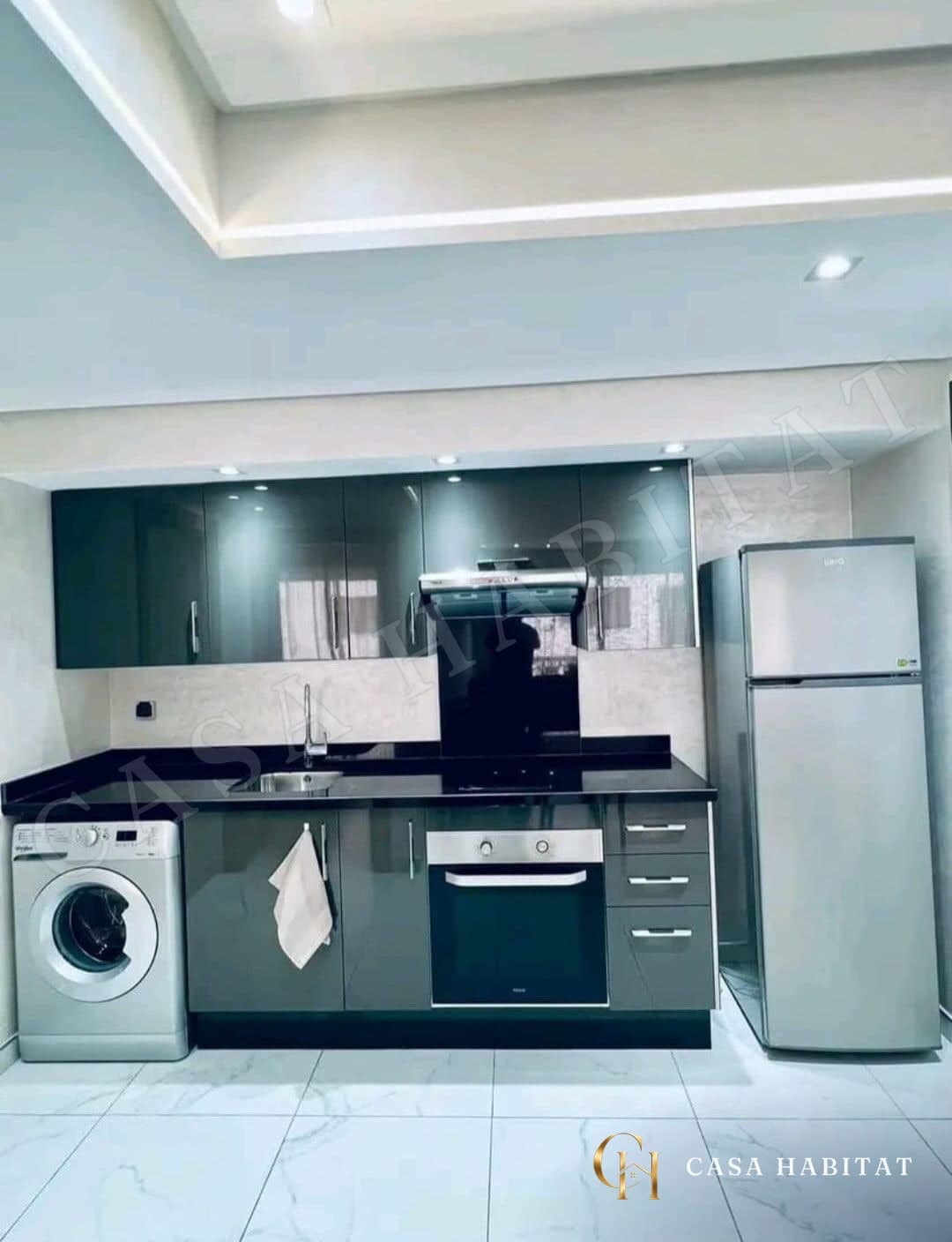 Cuisine grise avec plan noir, four, réfrigérateur et lave-linge