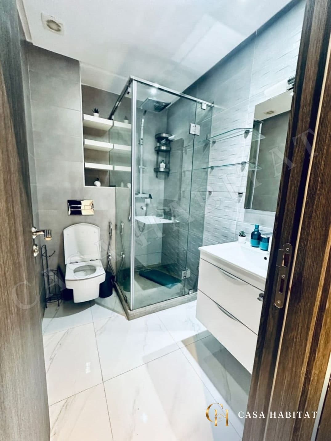 Salle de bain avec douche en verre, toilettes suspendues et vasque blanche
