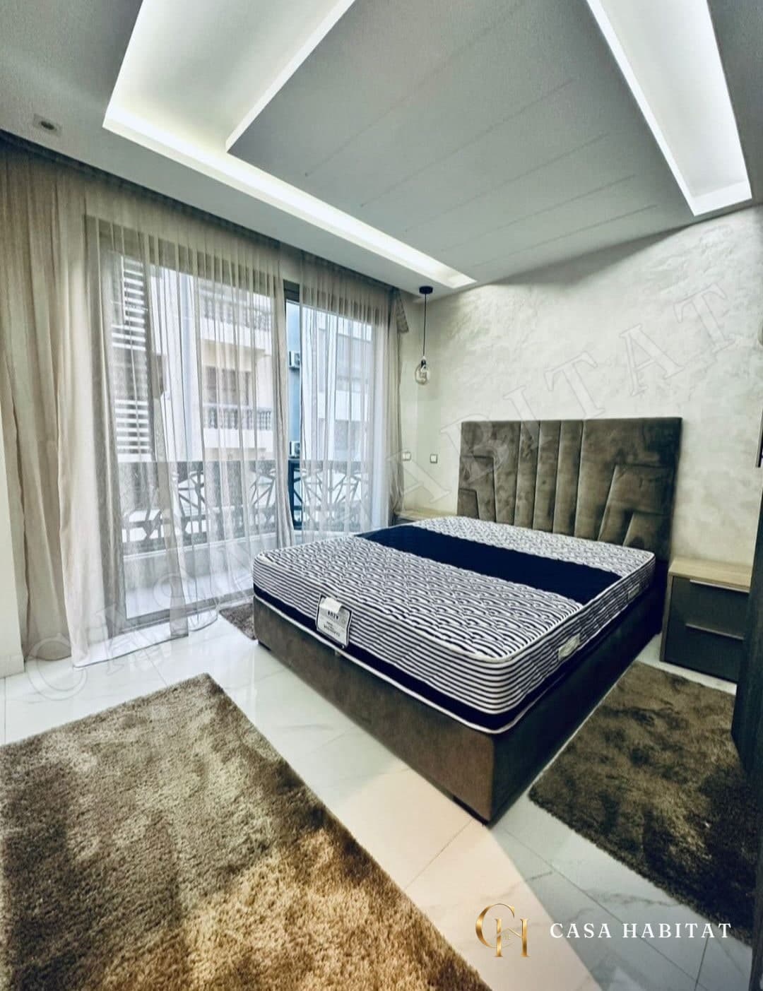 Chambre avec lit double, tapis en peau et rideaux voilage vers balcon