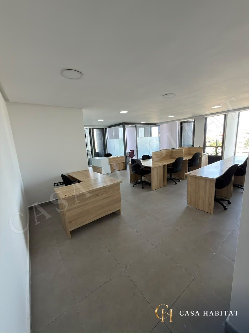 Oficina abierta con mesas de madera, sillas negras y mamparas de cristal