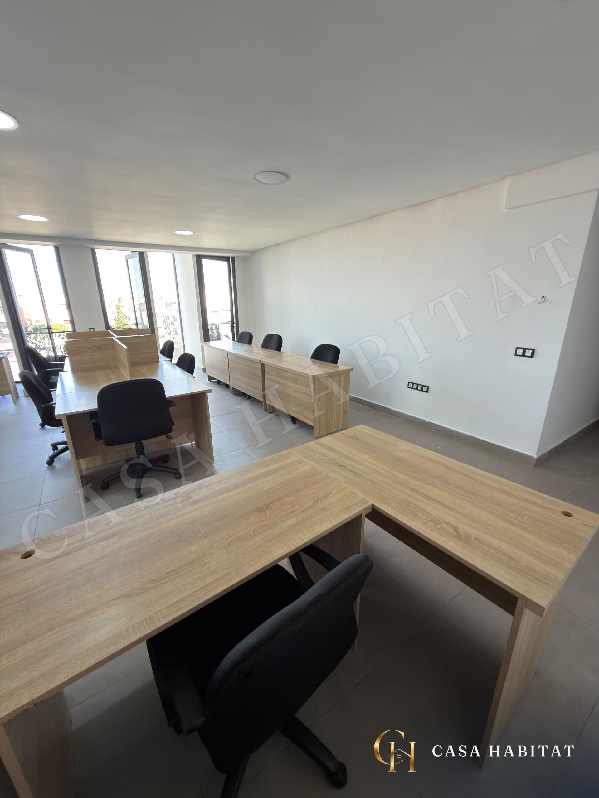 Espace de travail avec bureaux en bois et chaises noires près des fenêtres