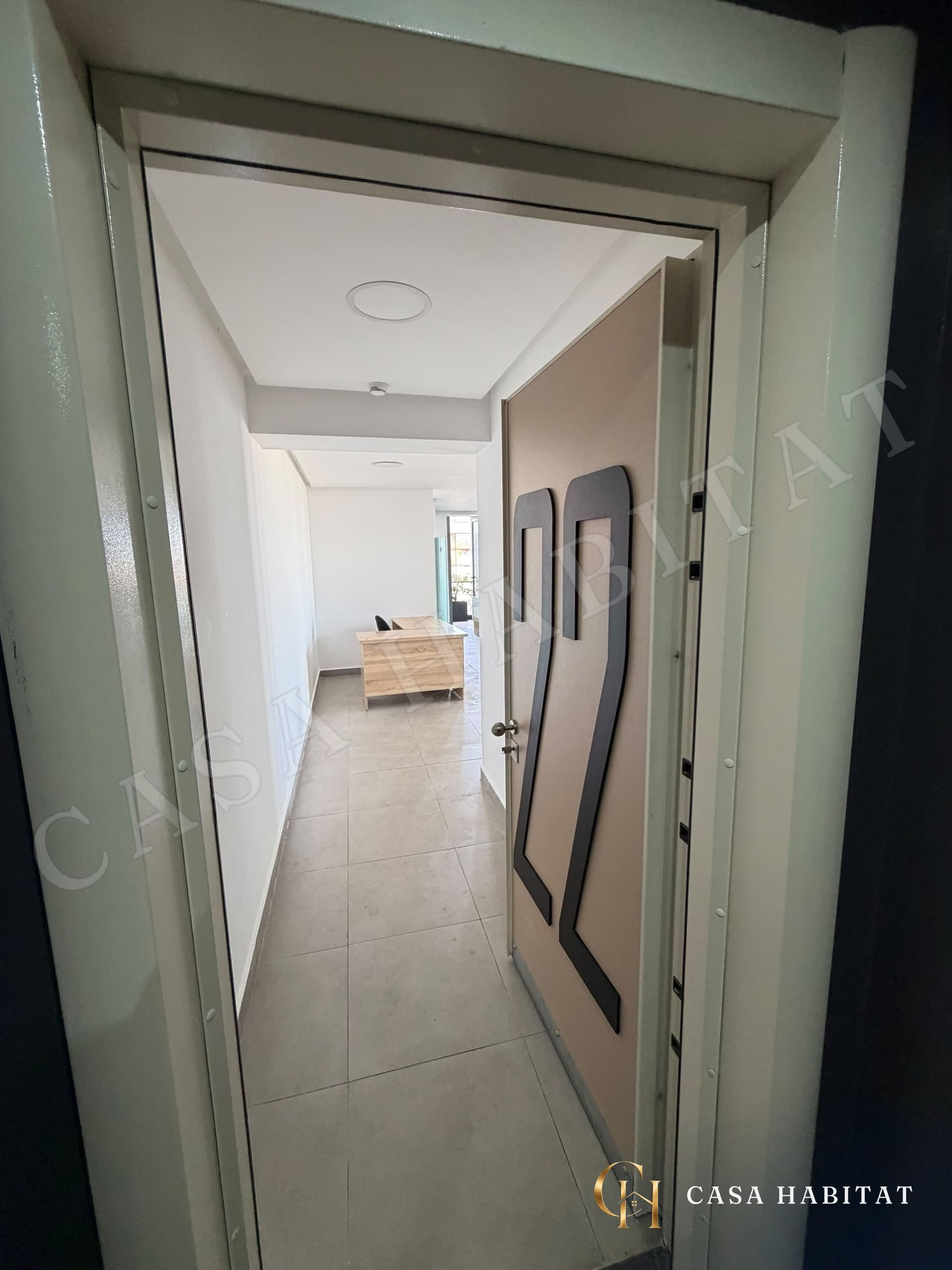 Entrée avec porte métallique menant à un couloir et un bureau