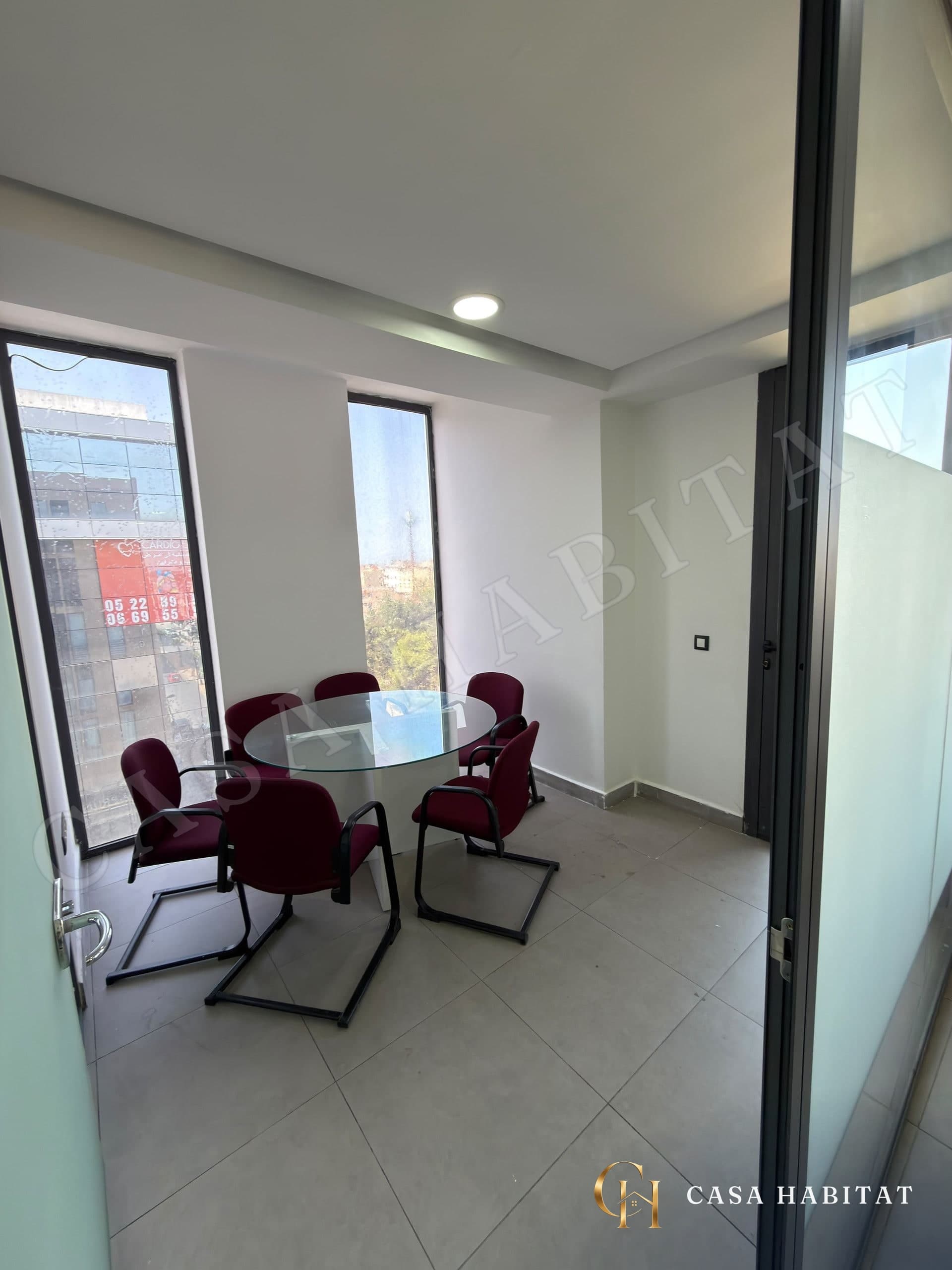 Salle de réunion avec table ronde en verre et chaises bordeaux