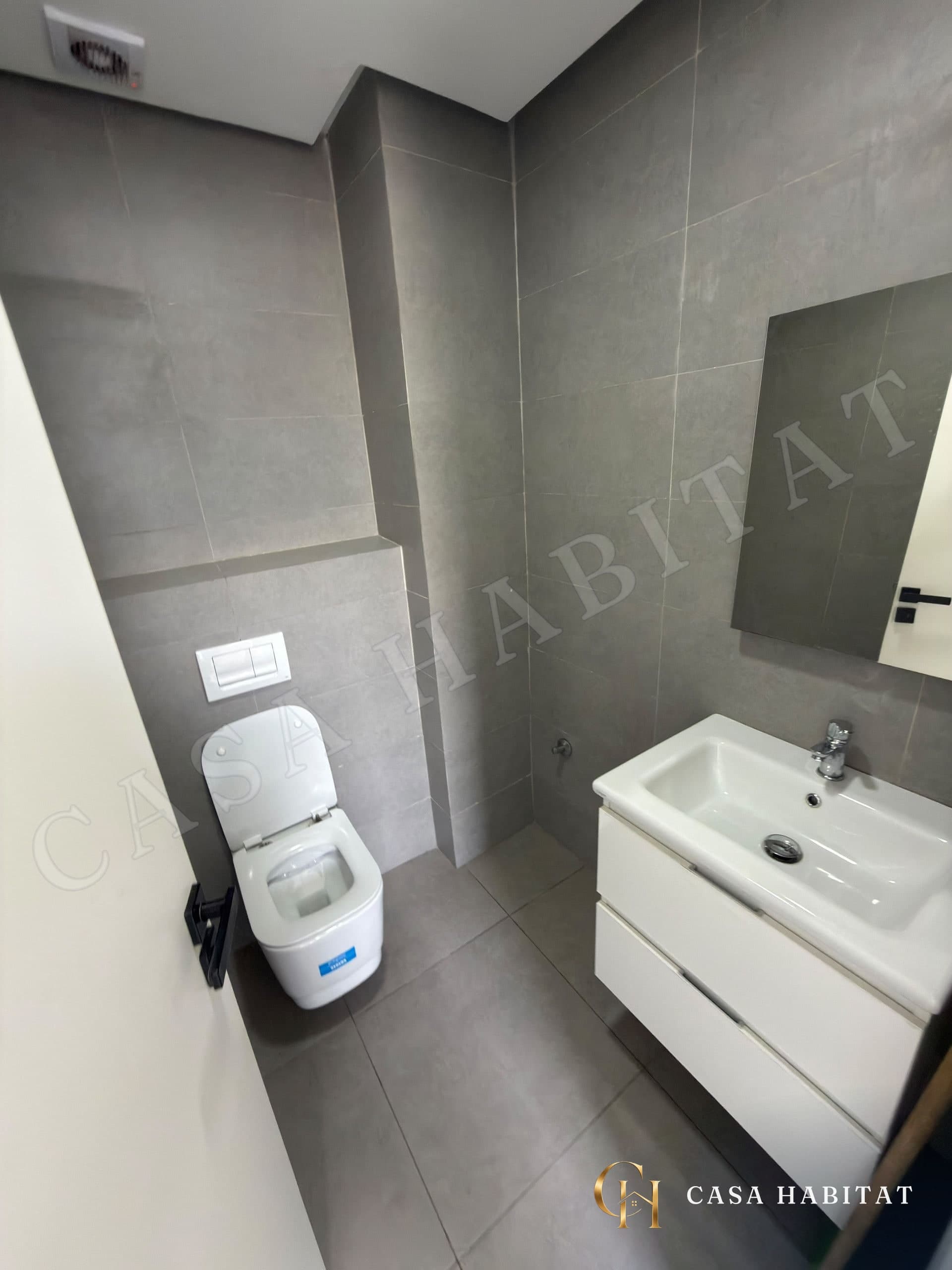 Salle d'eau avec WC suspendu, lavabo blanc et carrelage gris