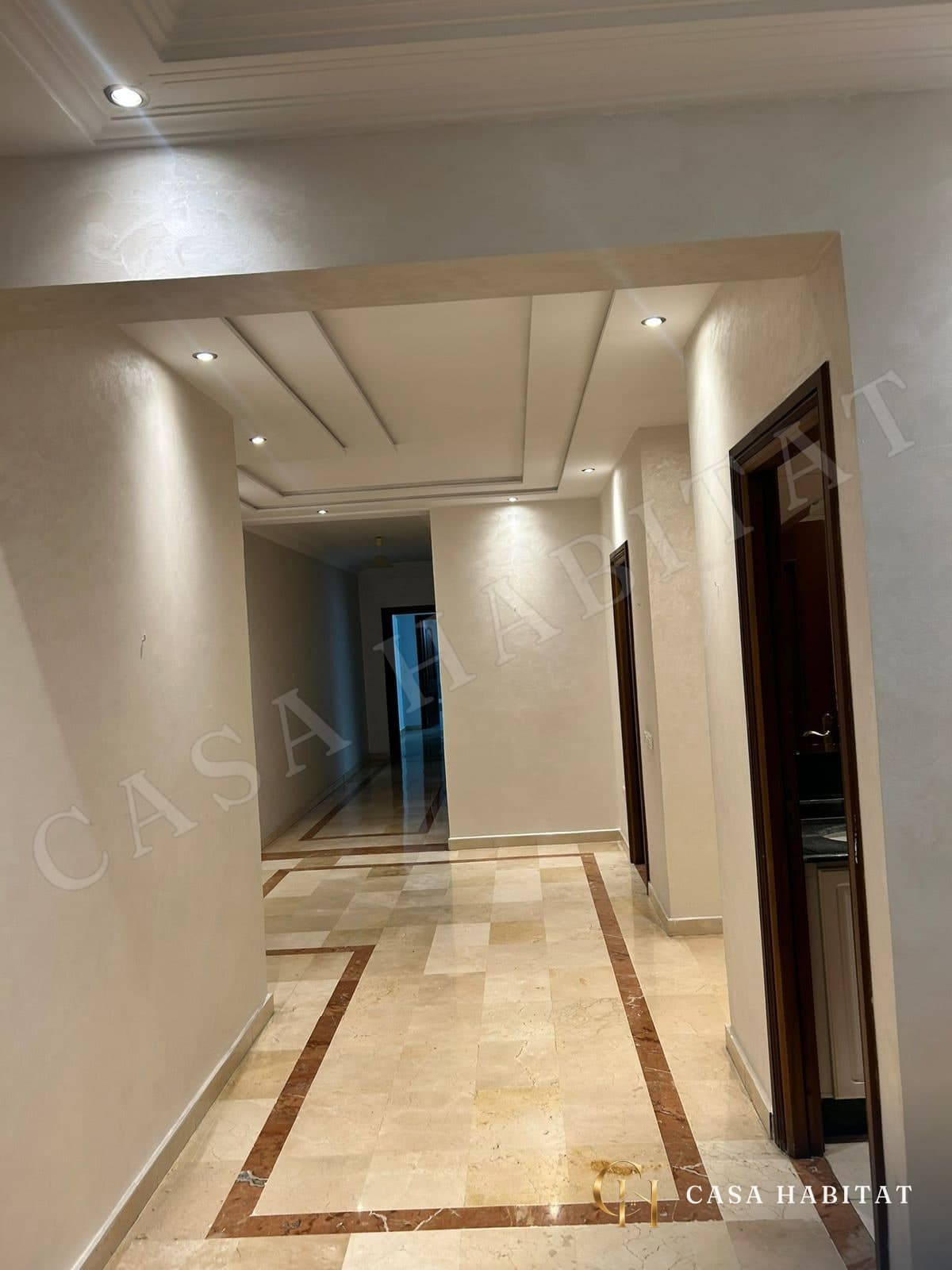 Couloir en marbre avec portes en bois et spots au plafond