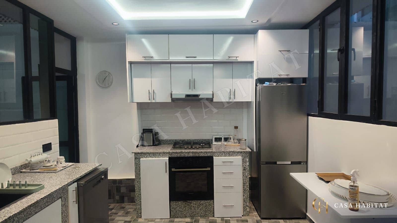 Cuisine blanche avec plan de travail en granit, four et réfrigérateur inox