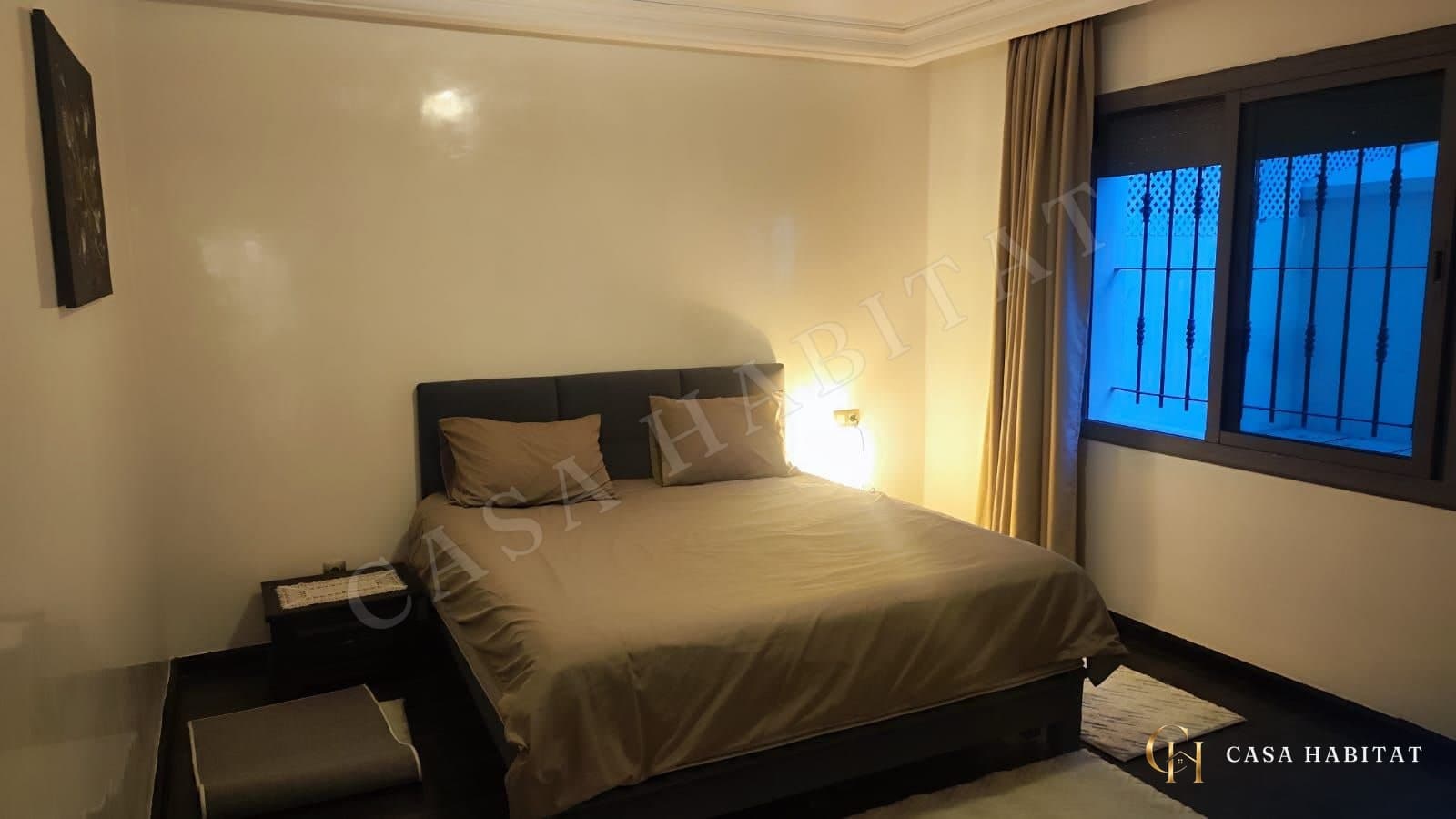 Chambre avec lit double, chevet sombre et lampe allumée