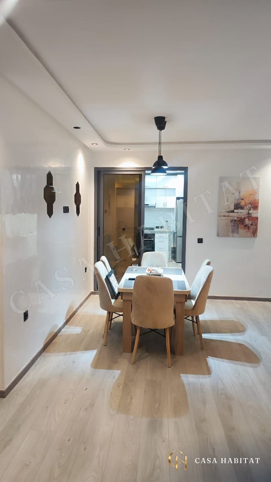 Salle à manger avec table et six chaises, cuisine visible au fond