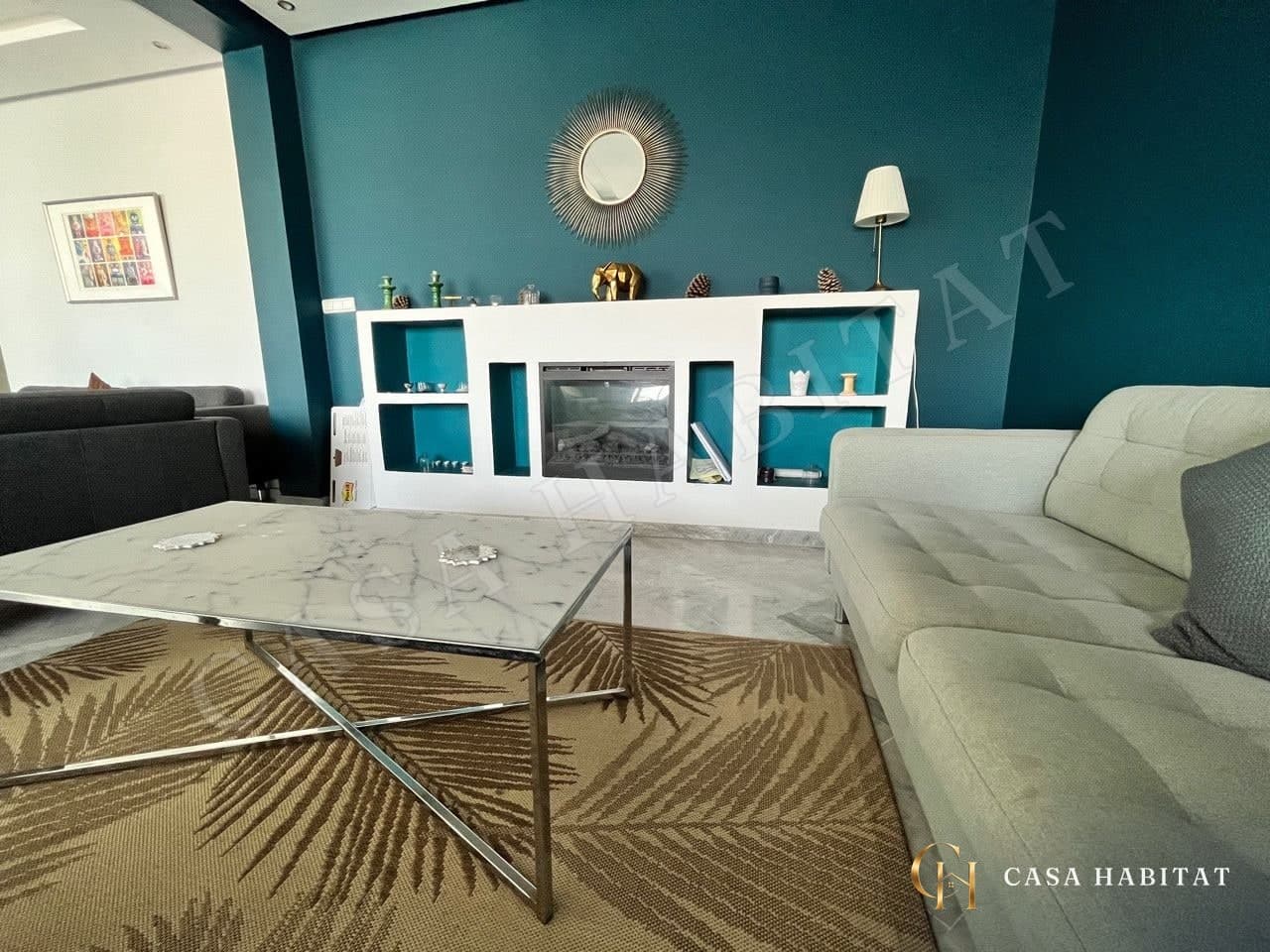 Salon avec canapé clair, table basse en marbre et cheminée électrique
