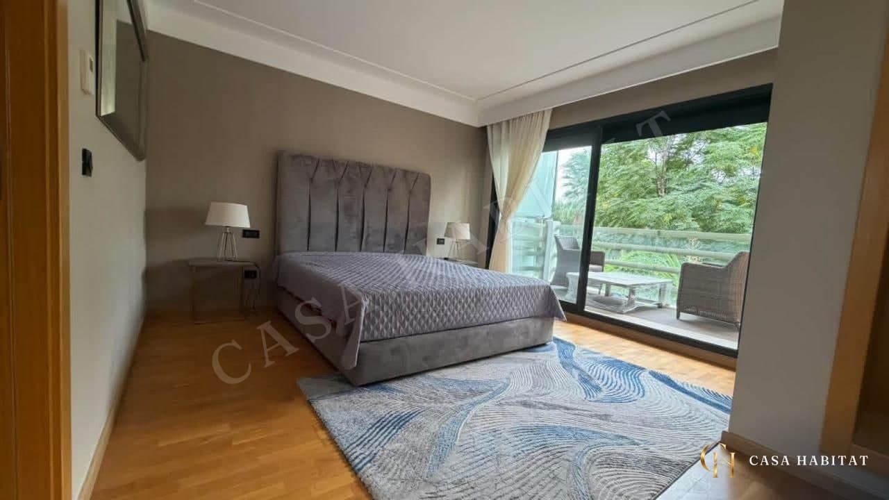 Chambre avec lit gris, tapis bleu et porte-fenêtre sur balcon