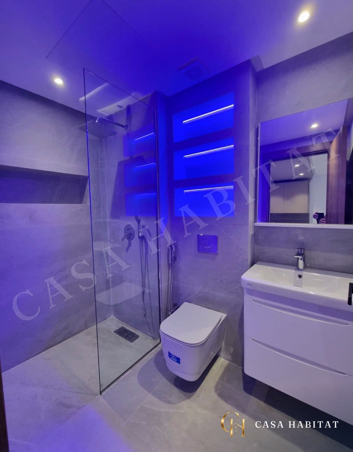 Salle de bain avec douche en verre, toilettes suspendues et éclairage bleu