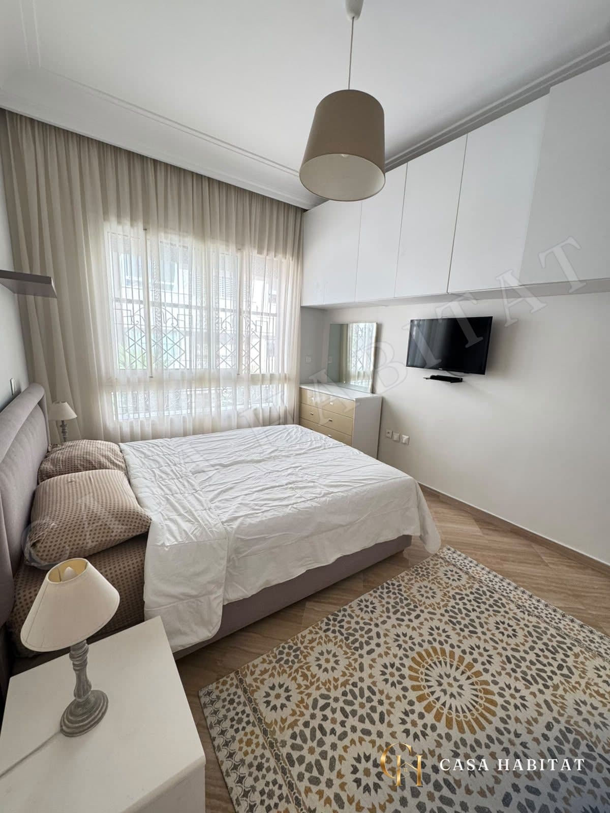Chambre avec lit blanc, rideaux clairs et tapis motifs