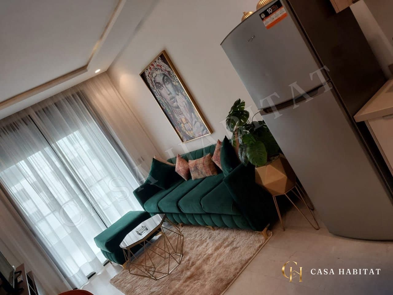 Salon avec canapé vert, tapis beige et réfrigérateur argenté