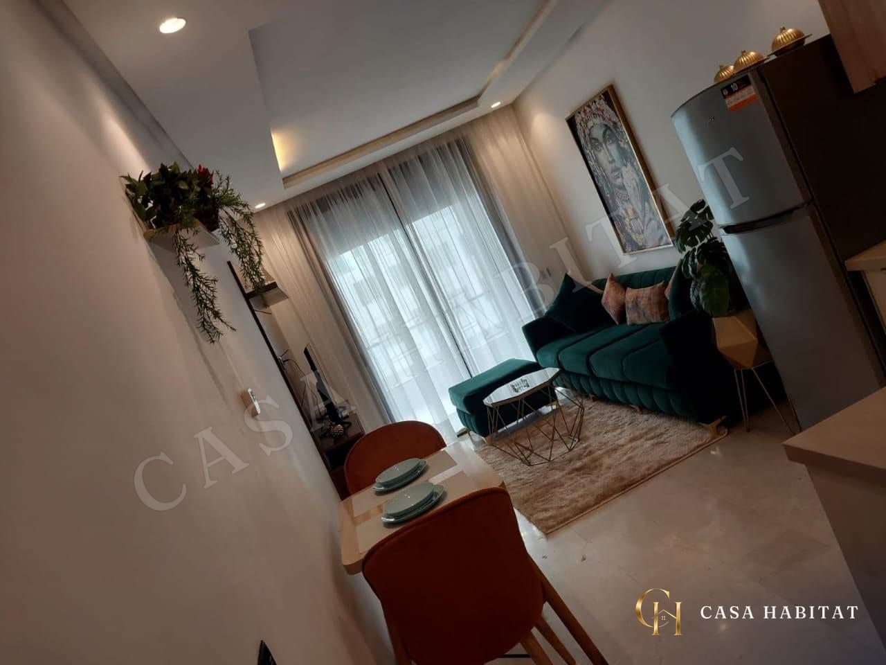 Salon avec canapé vert, tables basses dorées et rideaux translucides
