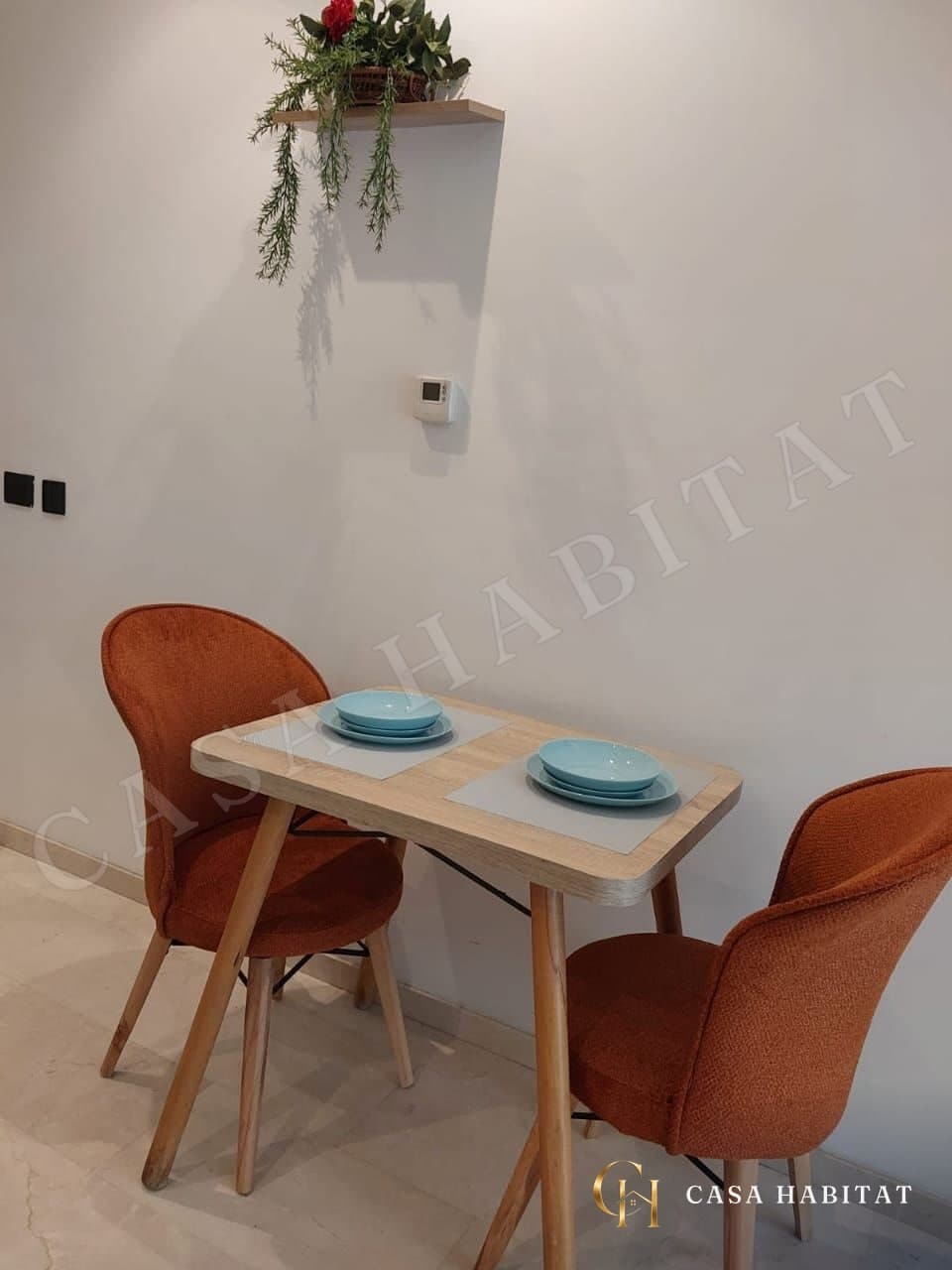 Coin repas avec table en bois, chaises orange et plante murale