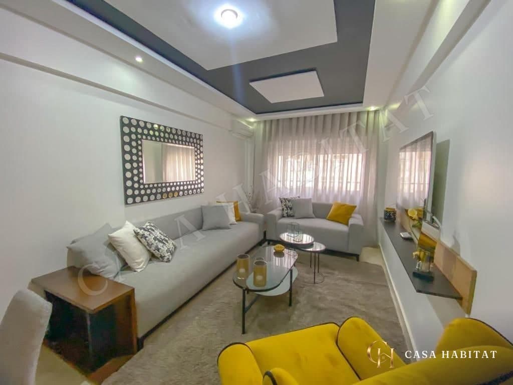Salon avec canapés gris, fauteuils jaunes et table basse en verre