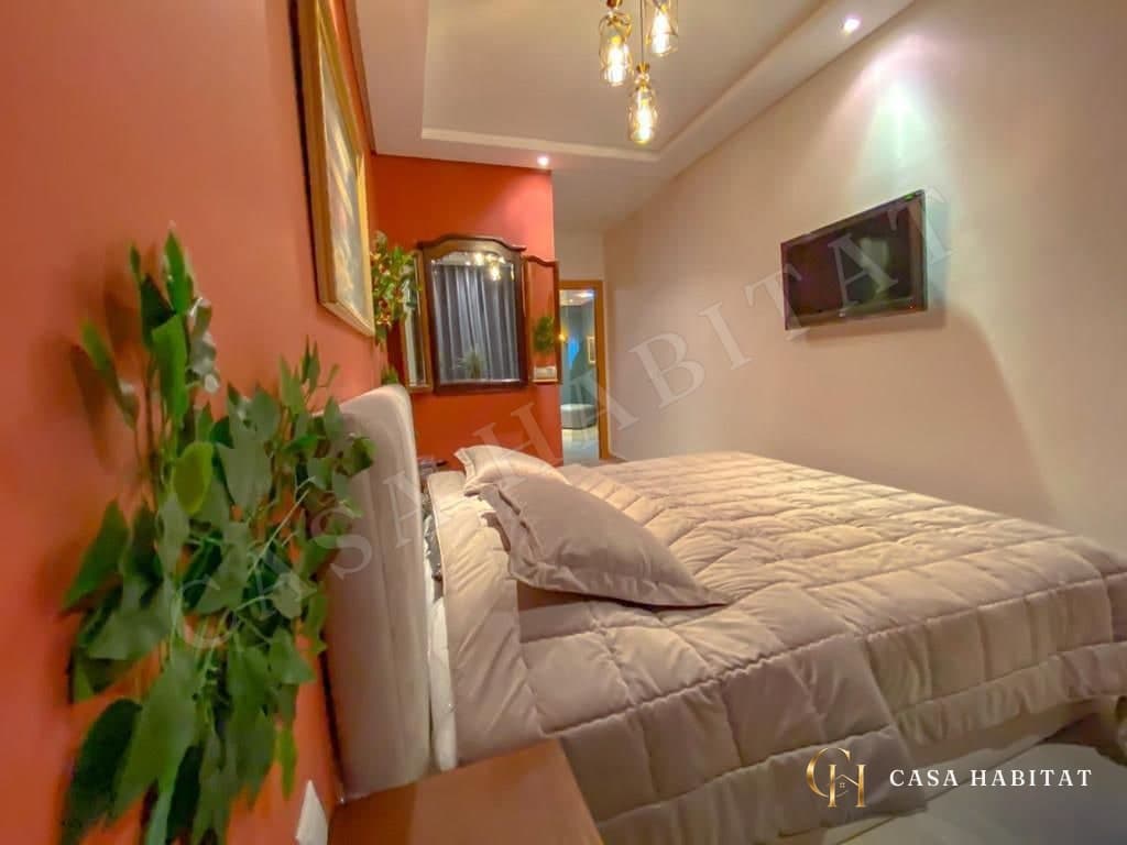 Chambre avec lit blanc, téléviseur mural et mur orange