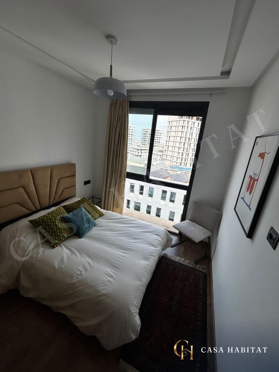 Chambre avec lit blanc, coussins colorés et grande fenêtre