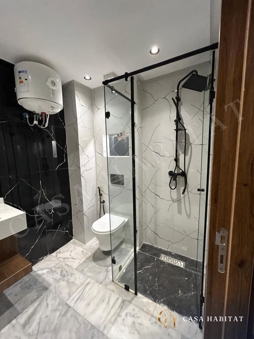 Salle de bain avec douche en verre, WC suspendu et chauffe-eau