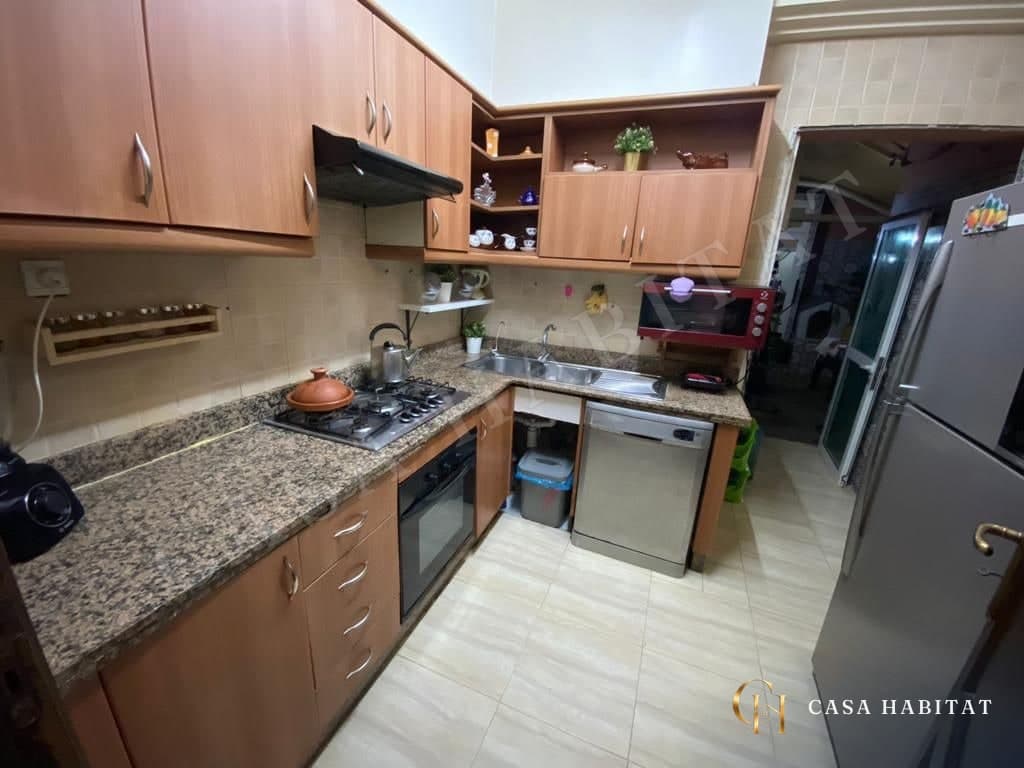 Cuisine équipée de placards en bois, plan de travail granit et plaque de cuisson